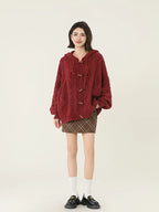 Woman standing with hands in pockets wearing a burgundy cable knit hooded cardigan and plaid mini skirt.