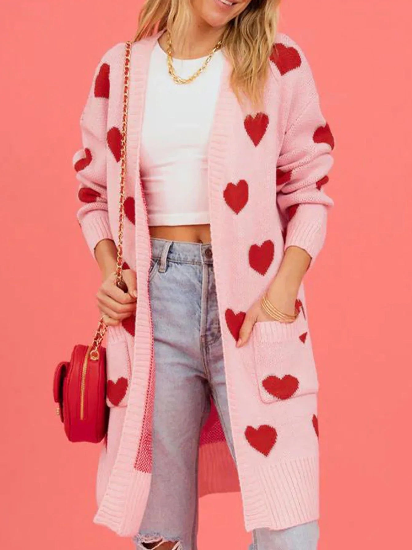 Front view of a woman in a pink heart-patterned cardigan, white crop top, and distressed denim jeans.