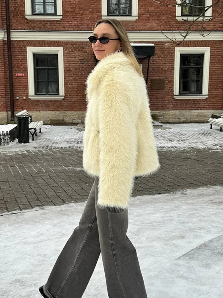 Woman in a cream faux fur jacket and grey jeans walking in the snow.