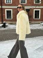 Woman in a cream faux fur jacket and grey jeans walking in the snow.