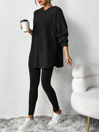 Woman wearing a black ribbed knit loungewear set consisting of a hooded tunic and leggings, holding a coffee cup.