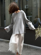 Woman in a grey oversized knit sweater and white skirt, with arms outstretched, holding dried flowers.