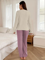 Woman from the back wearing a cream long-sleeve pajama top with a pink heart graphic and "love you" text, and matching ribbed purple pajama pants.