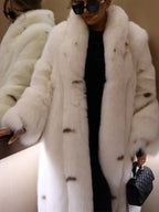 Woman in a white faux fur coat and black outfit, holding a black quilted handbag, with large sunglasses.