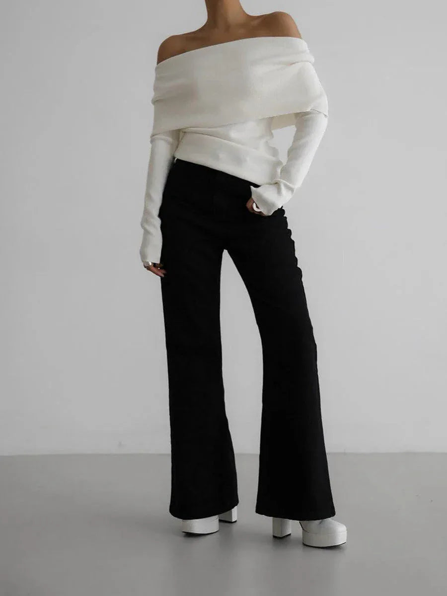 Full body shot of a woman wearing a white off-the-shoulder sweater and black flared pants.