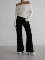 Full body shot of a woman wearing a white off-the-shoulder sweater and black flared pants.
