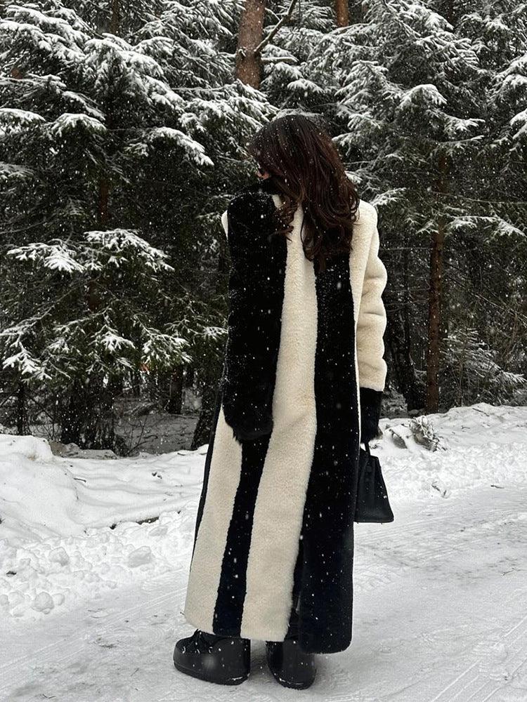 Woman from behind, showcasing the bold vertical stripe pattern of her black and white faux fur coat in a snowy woodland.