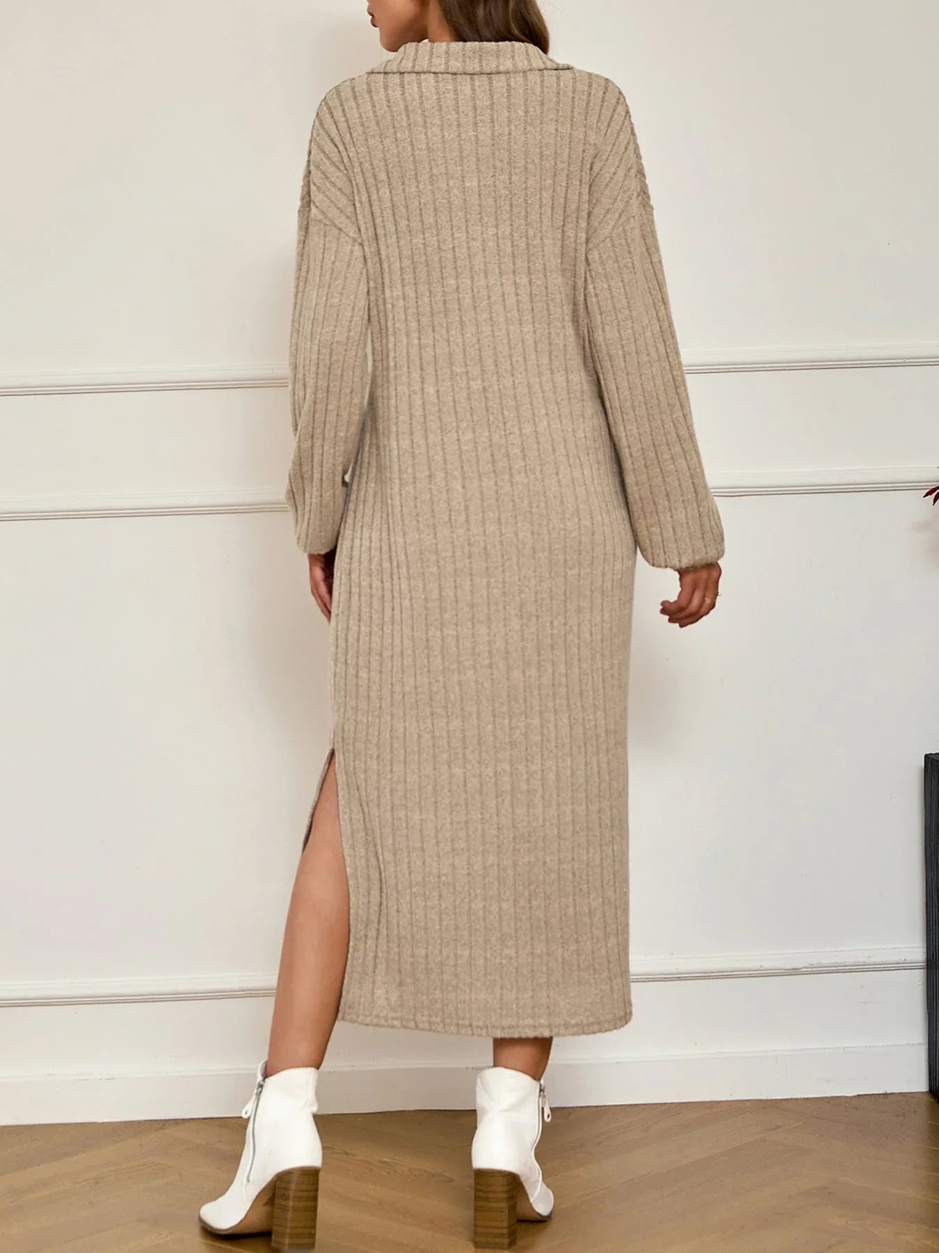 Back view of a woman wearing a beige ribbed knit midi dress with a collared V-neck and long sleeves, showcasing a side slit.