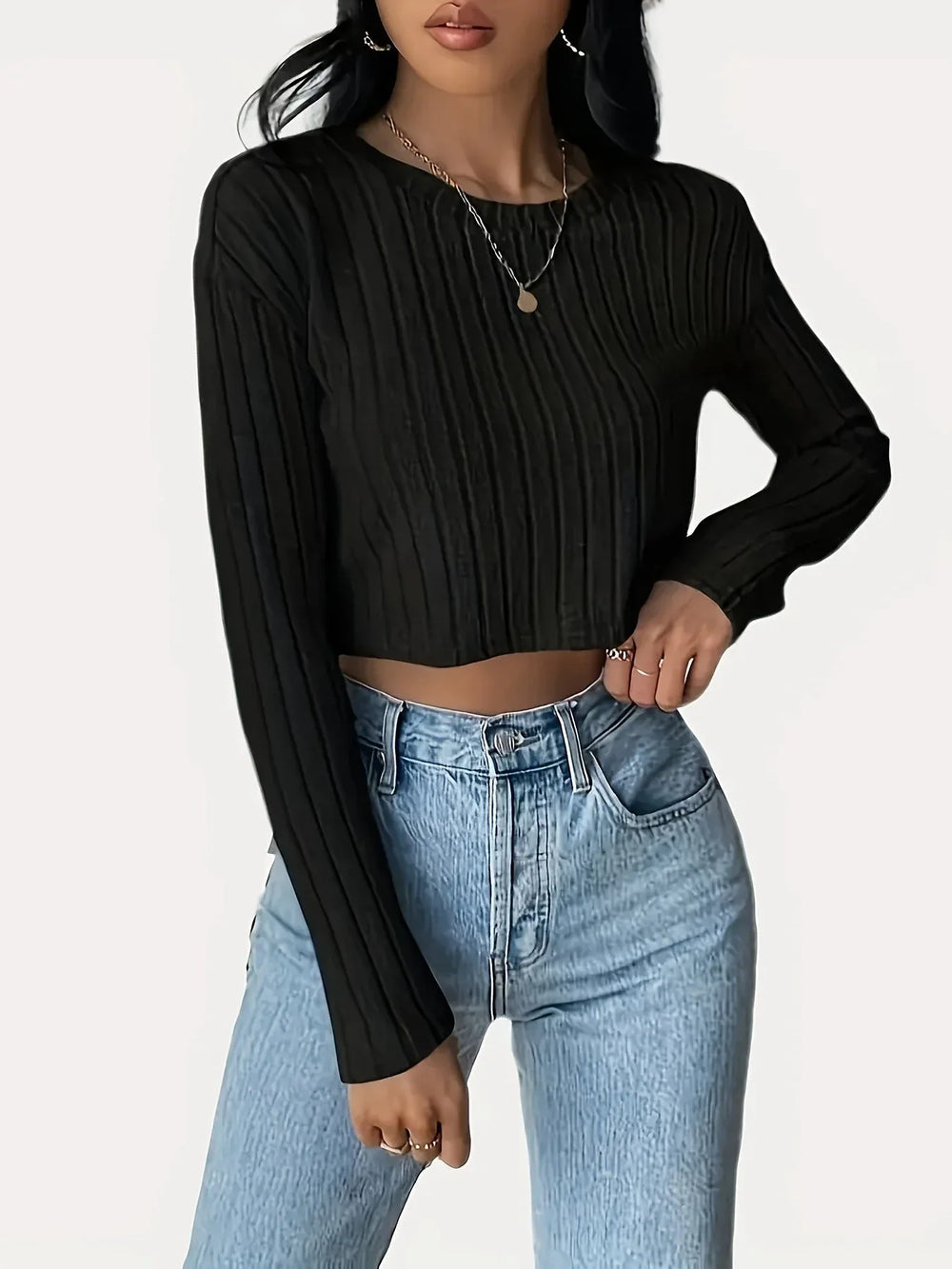 Woman wearing a black ribbed long-sleeve cropped top and light wash high-waisted jeans, posing with one hand on her hip.