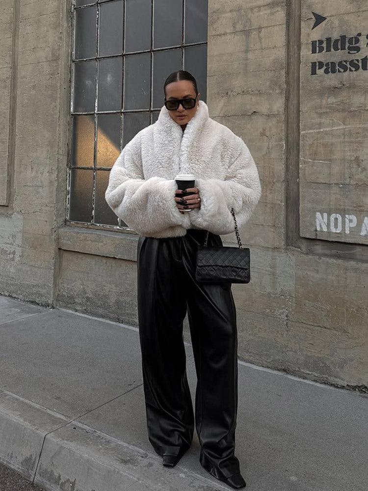 woman wearing a white faux fur jacket and black leather pants holding a coffee cup