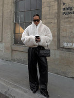 woman wearing a white faux fur jacket and black leather pants holding a coffee cup