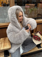 Woman sitting with a coffee and a bouquet of roses, wearing a grey faux fur hooded coat