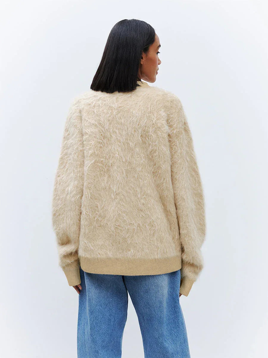Back view of a woman wearing a beige fuzzy V-neck button-up cardigan with two front pockets.