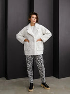 Full length shot of a model in a white textured faux fur jacket with hands in pockets, styled with zebra print pants.