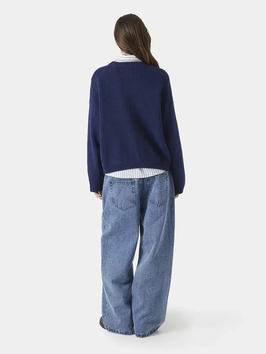 back view of a woman wearing a navy blue crew neck sweater with red "EME STUDIOS" embroidery Secondary image