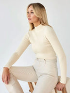 Woman wearing a cream ribbed mock neck cropped sweater and cream cargo pants, sitting in a chair, profile view.