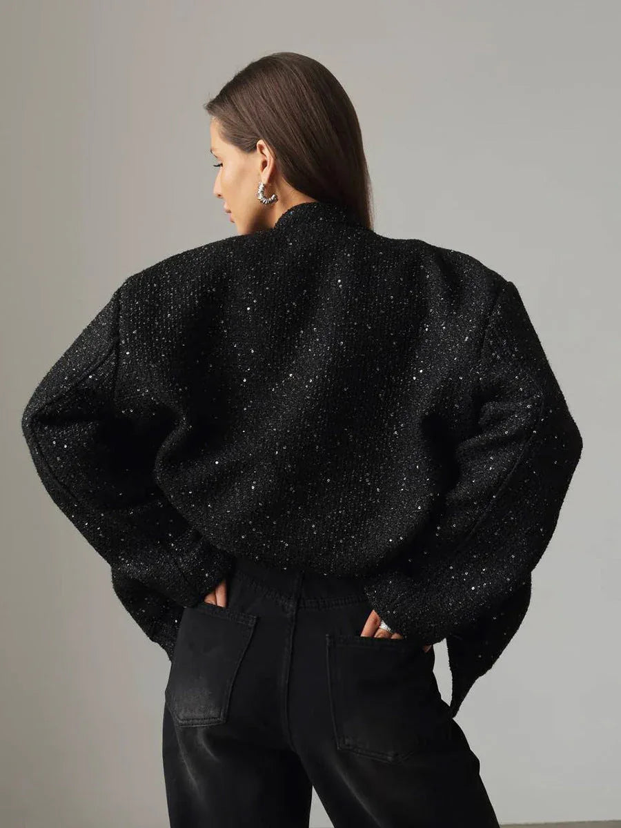 Back view of a woman wearing a black sparkly tweed cropped jacket and black wide-leg jeans, hands in pockets.