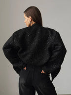 Back view of a woman wearing a black sparkly tweed cropped jacket and black wide-leg jeans, hands in pockets.