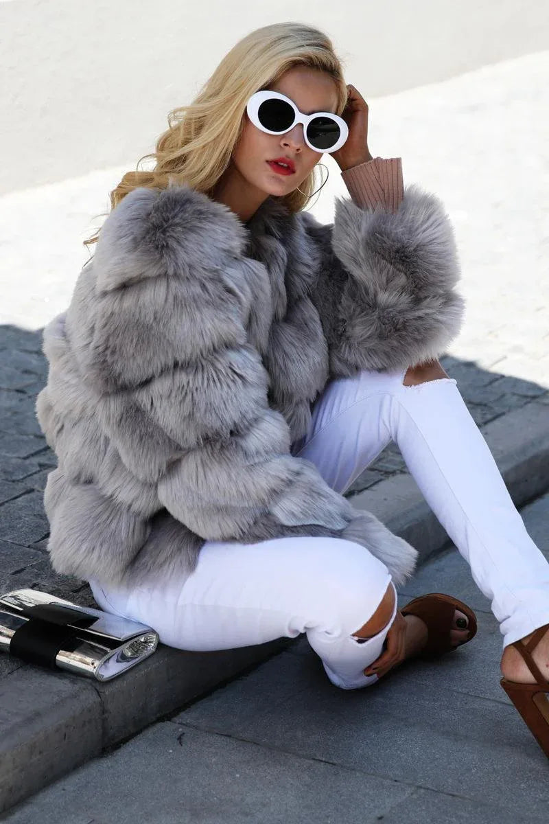 Woman sitting on the ground in a grey faux fur jacket and ripped white jeans
