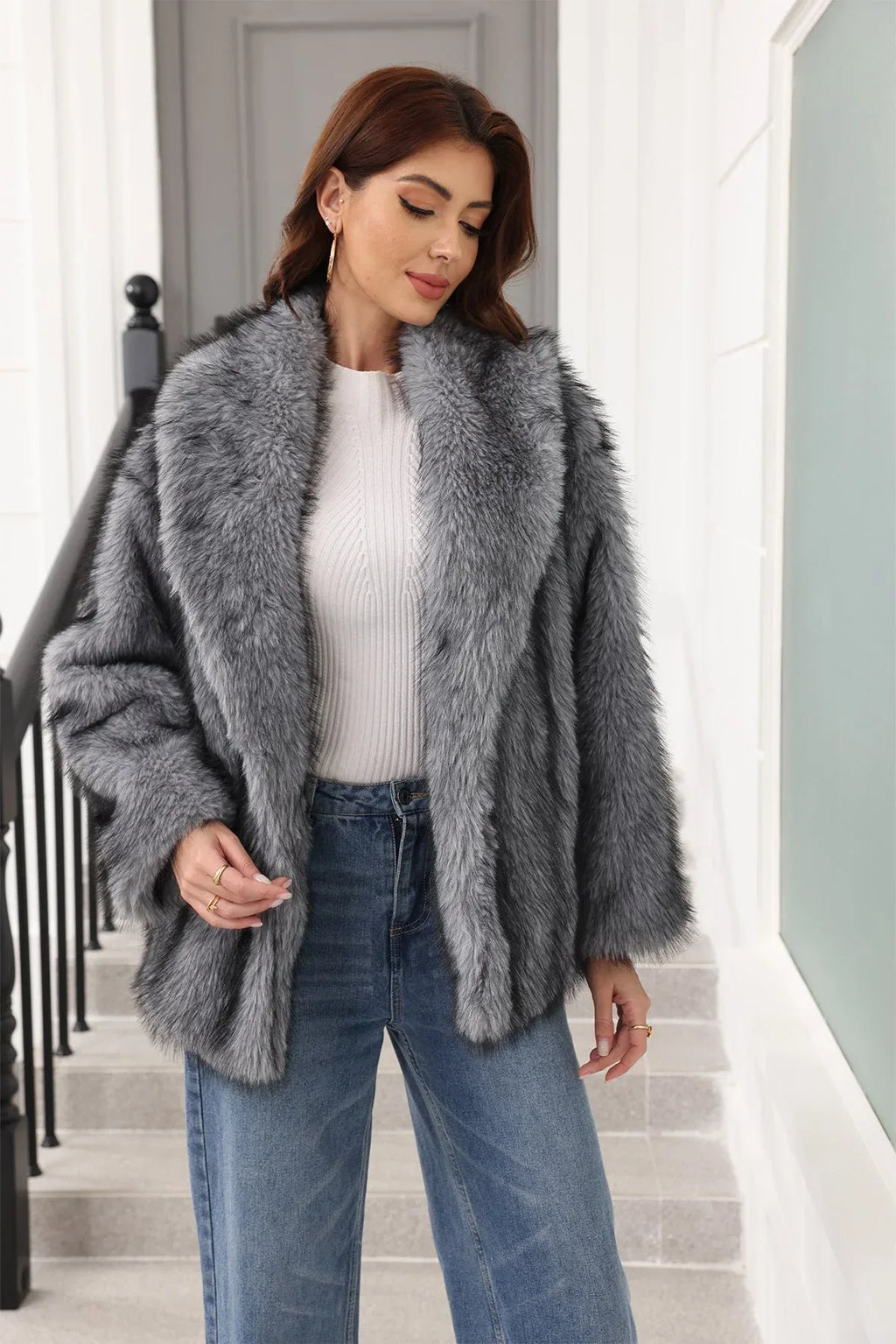 Woman in a grey faux fur jacket and white top, looking down.