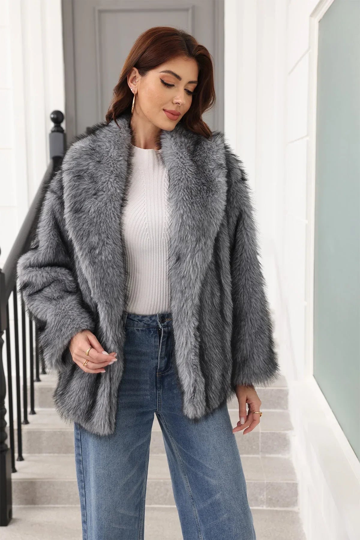 Woman in a grey faux fur jacket and white top, looking down.