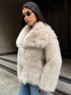 Close-up of a woman wearing a cream-colored faux fur jacket with a large collar, blue jeans, and sunglasses.