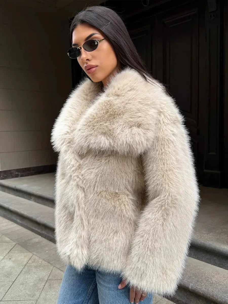Close-up of a woman wearing a cream-colored faux fur jacket with a large collar, blue jeans, and sunglasses.