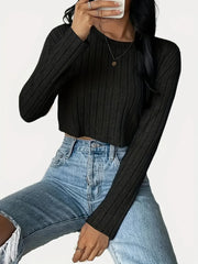 Woman wearing a black ribbed long-sleeve cropped top and light wash high-waisted jeans, sitting down with legs crossed.