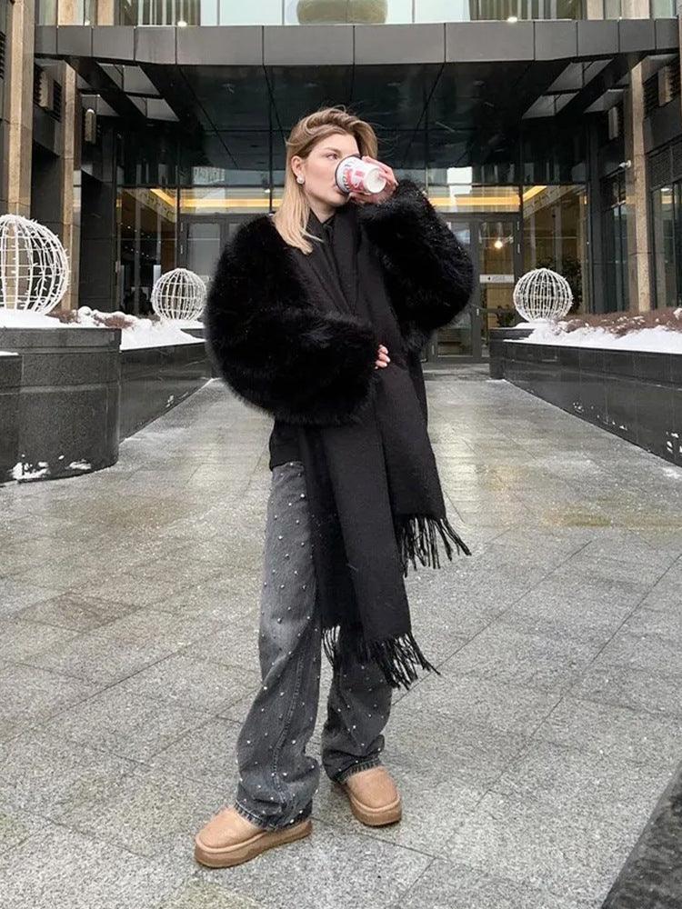 Woman wearing a black faux fur jacket and studded jeans, holding a coffee cup outdoors