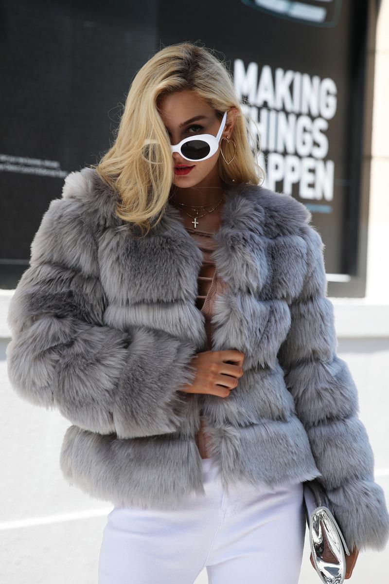 Woman wearing a grey faux fur jacket with white pants and sunglasses