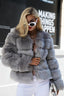 Woman wearing a grey faux fur jacket with white pants and sunglasses