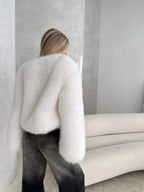 Back view of a woman wearing a white fluffy faux fur cropped jacket and dark wash jeans.