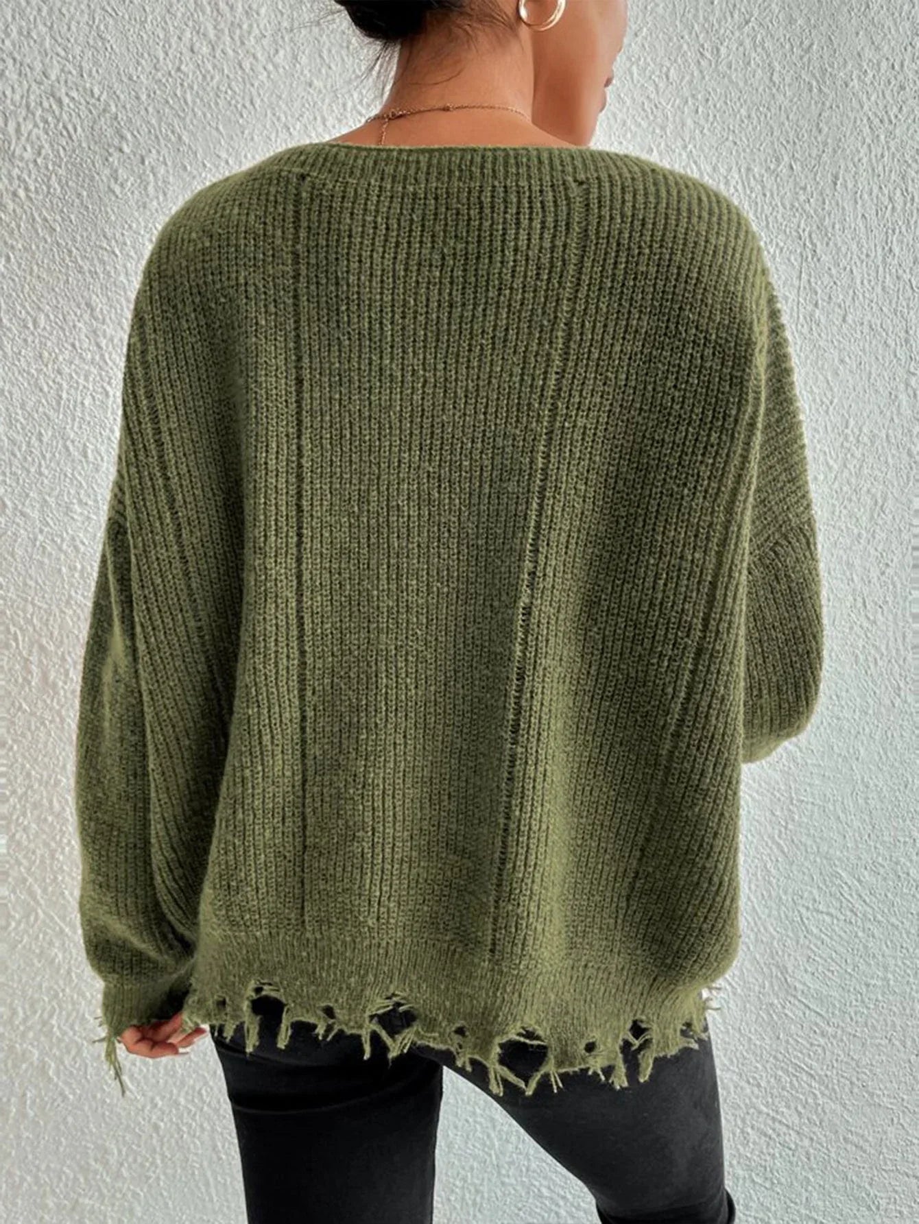 Back view of a woman wearing a green oversized distressed knit sweater with black pants