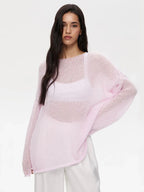 Woman wearing a light pink sheer knit sweater and white pants, standing against a white background.