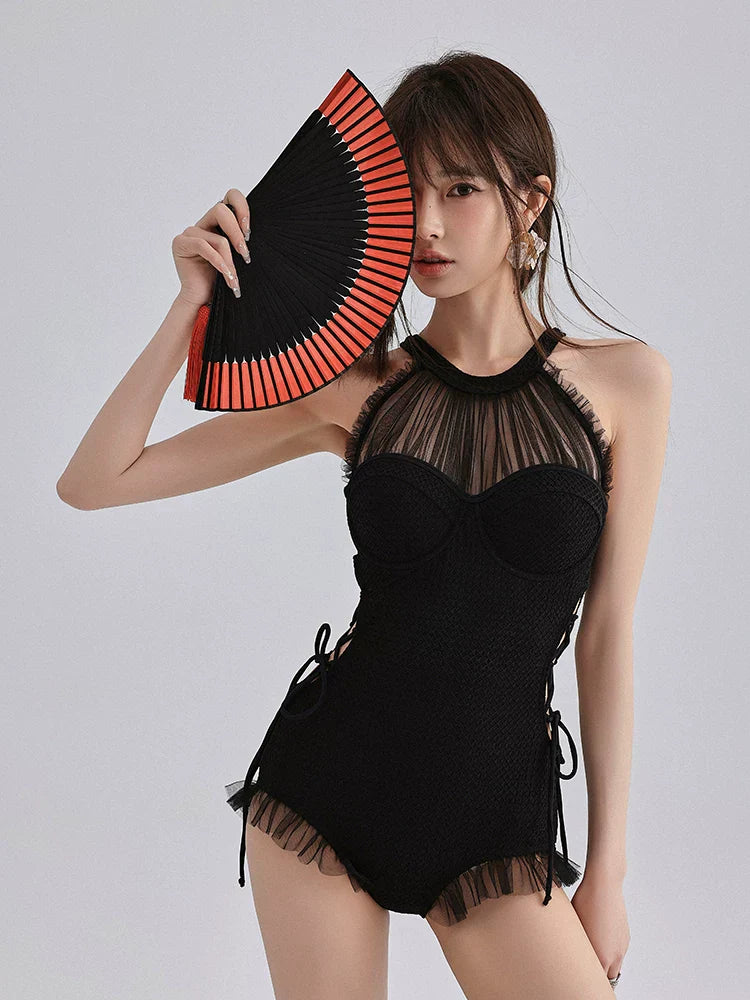 Woman in a black one-piece swimsuit, holding a red and black fan to her face