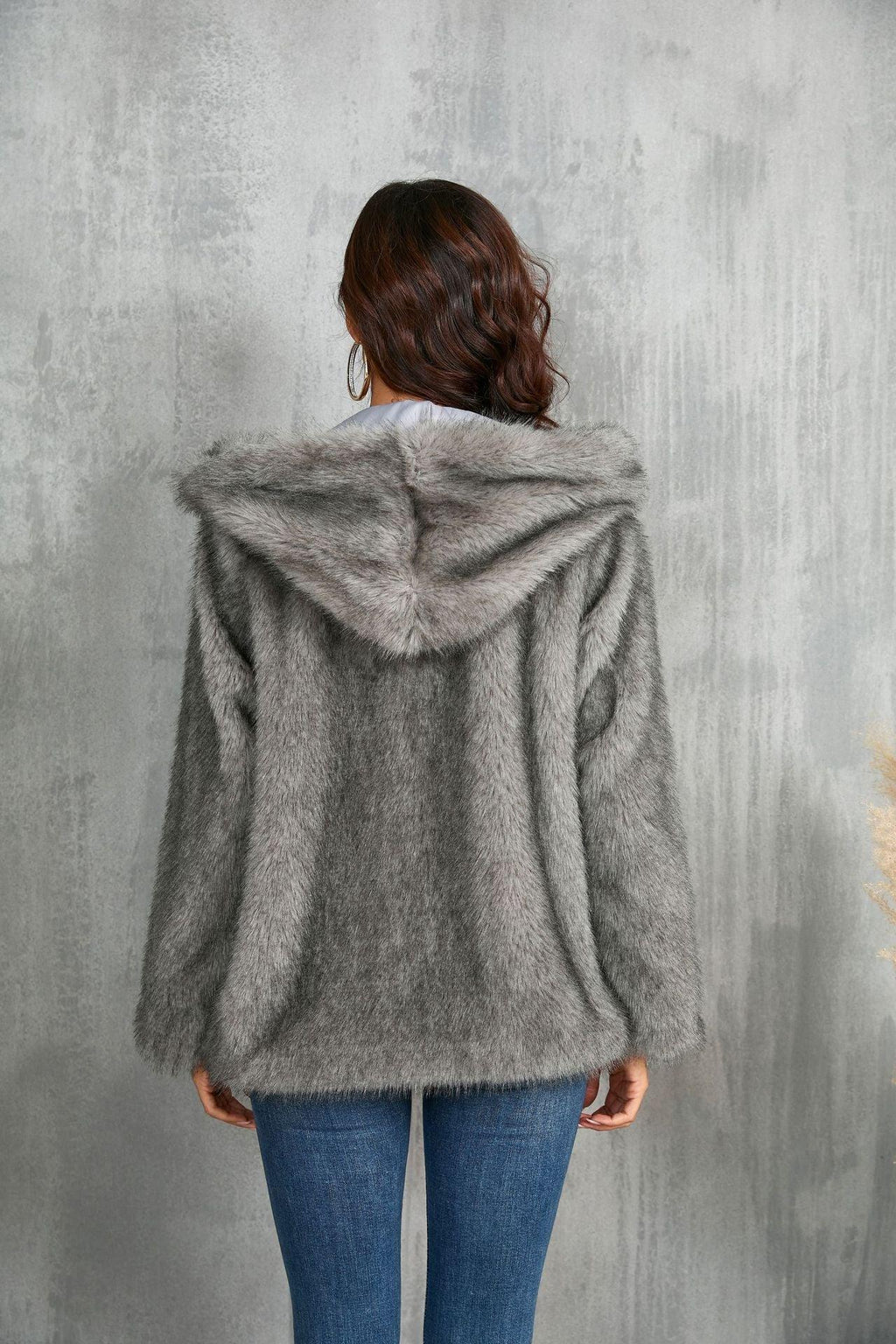 Woman wearing a gray faux fur hooded jacket with blue jeans, seen from the back.