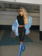 Woman walking in a light blue faux fur jacket, black crop top, black shorts, and blue and silver lace-up boots.