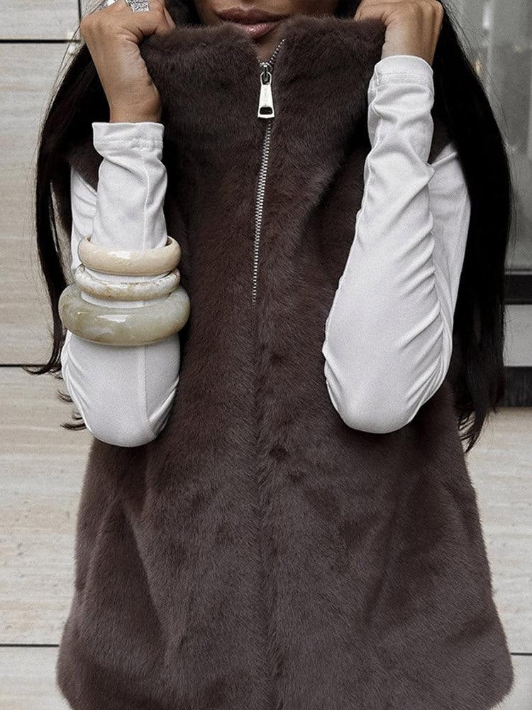 Front view of a woman wearing a brown faux fur vest with a zipper closure and a white long-sleeved shirt.