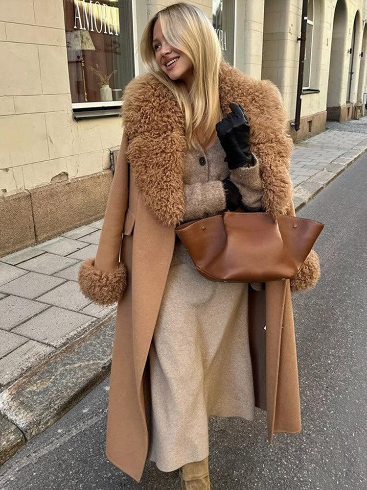 Woman wearing a long camel wool coat with a brown faux fur collar and cuffs, holding a brown handbag. Main image
