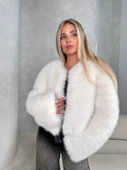 Woman wearing a white fluffy faux fur cropped jacket with dark wash jeans, looking to the side.