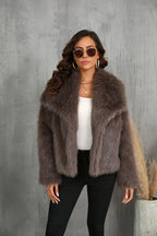 Woman wearing a brown faux fur jacket, white top, and black pants, holding sunglasses.