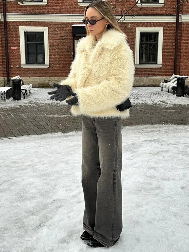Woman wearing a cream faux fur jacket and grey wide-leg jeans standing in the snow. Main image