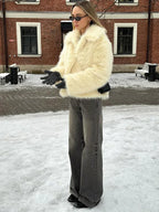 Woman wearing a cream faux fur jacket and grey wide-leg jeans standing in the snow.