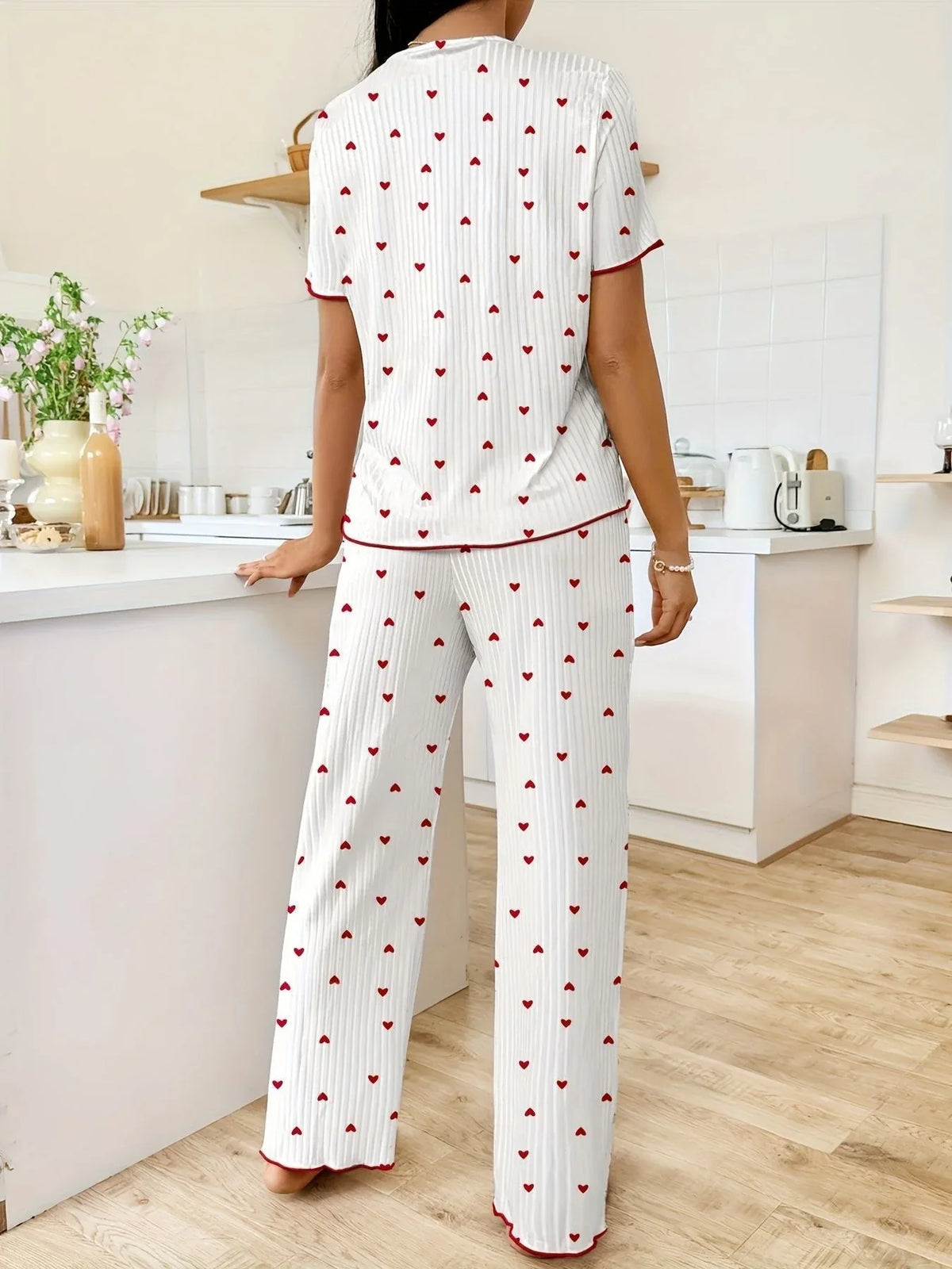 Woman wearing white and red heart print pajama set, standing with back to camera in a kitchen