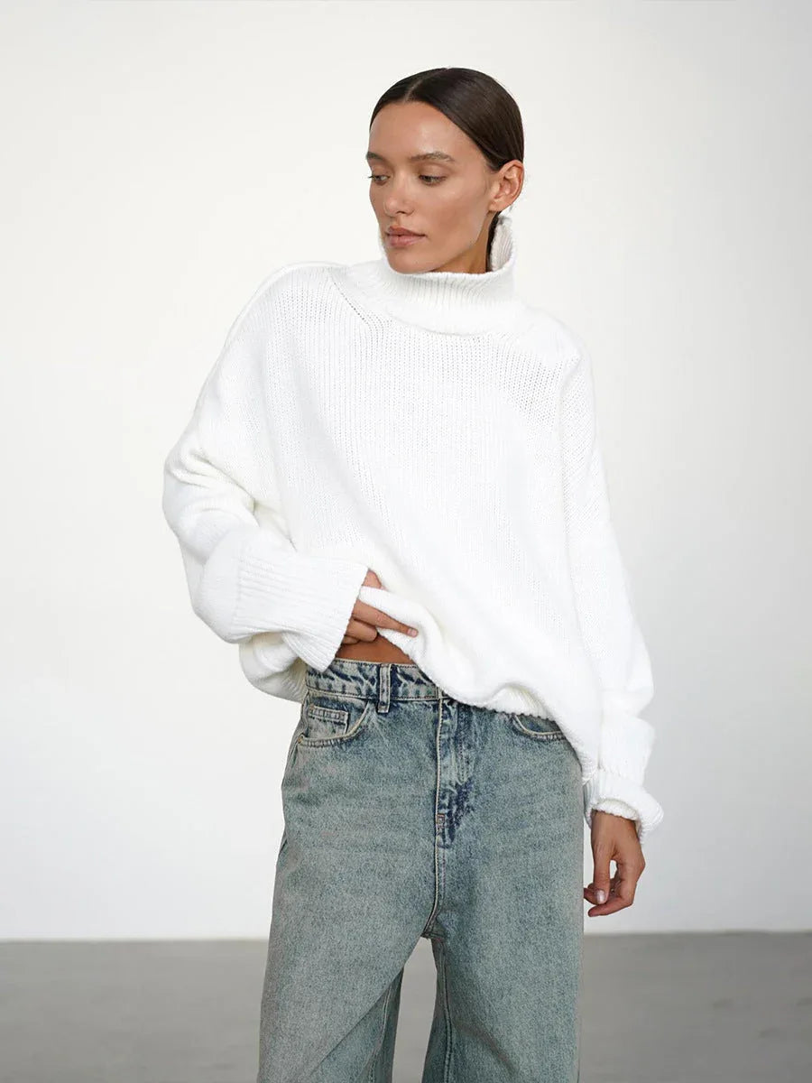 Close-up of a woman wearing an oversized white turtleneck sweater, lifting the hem to show her jeans.