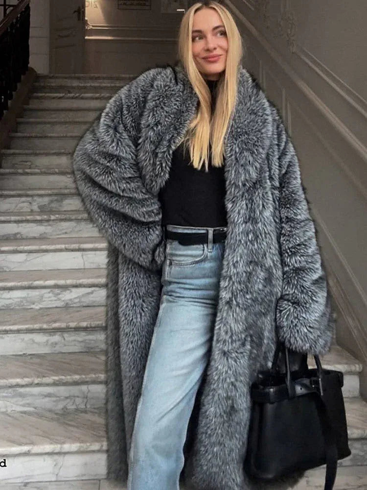 Woman wearing a long grey faux fur coat with a black turtleneck and blue jeans, standing on marble stairs. Main image