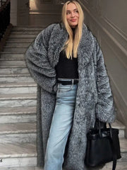 Woman wearing a long grey faux fur coat with a black turtleneck and blue jeans, standing on marble stairs.