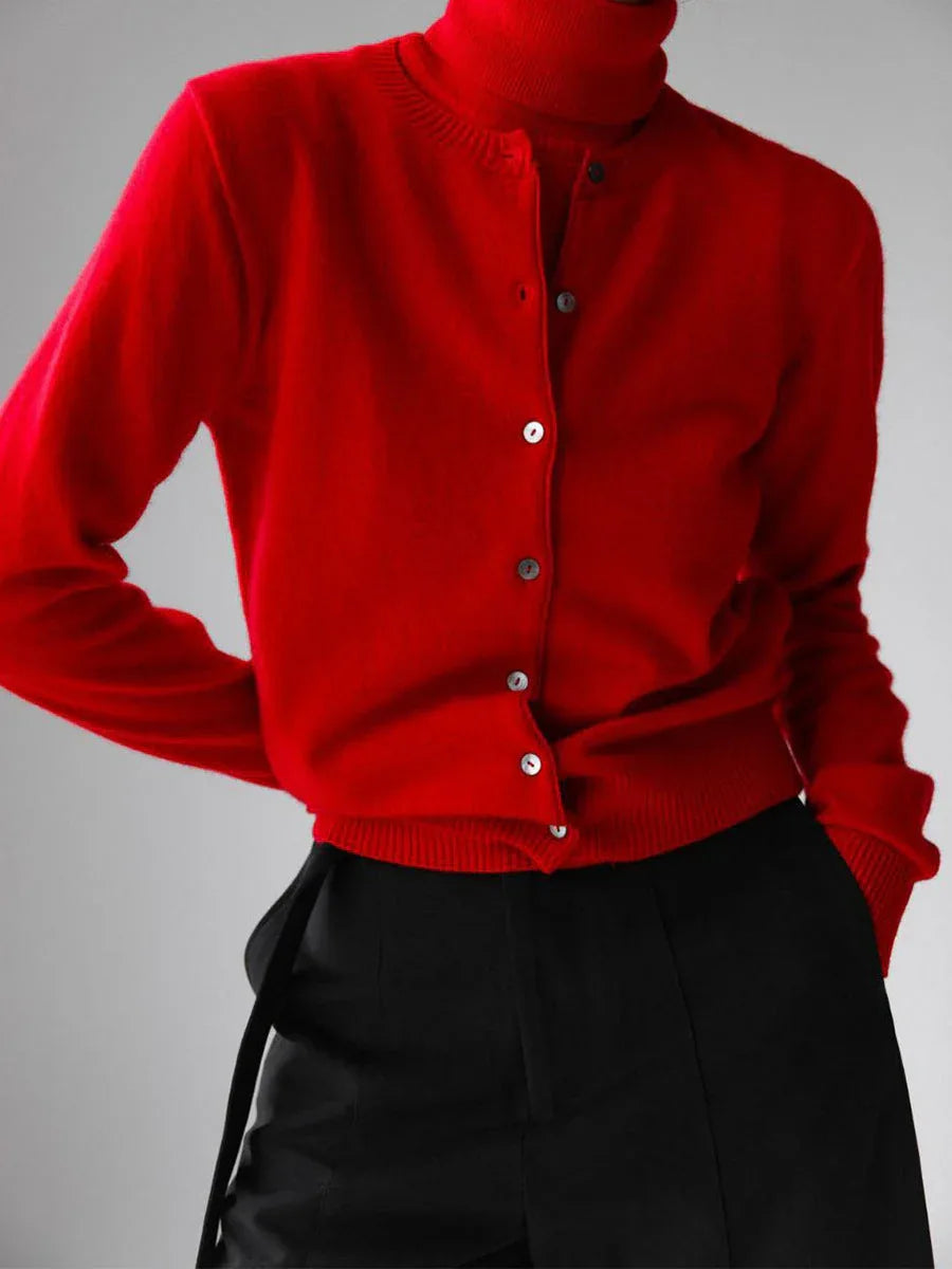 Close-up of a woman wearing a red cashmere cardigan over a red turtleneck and black trousers.
