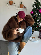 woman wearing a brown faux fur coat with jeans and a baseball cap, holding a coffee cup