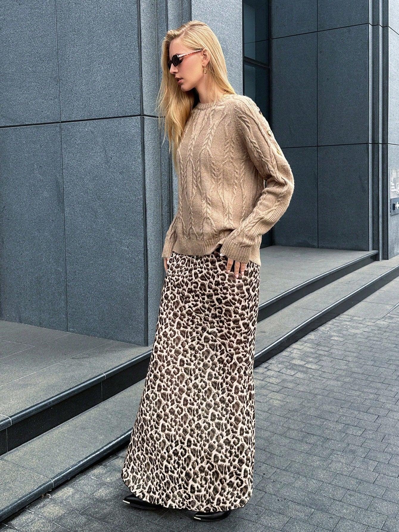 Woman posing in a tan cable knit sweater and leopard print maxi skirt, with hands in pockets.